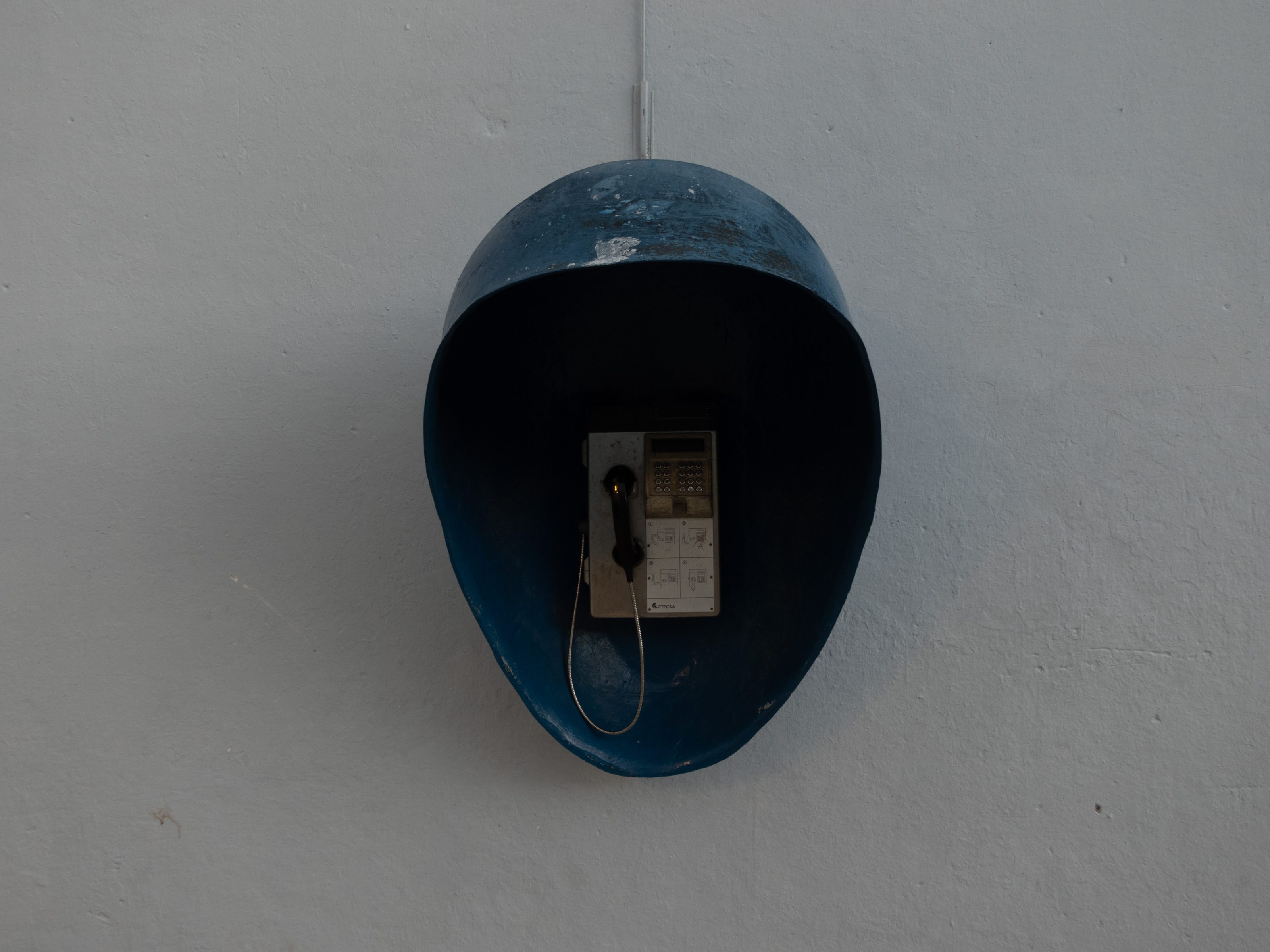 A vintage public payphone mounted on a wall, encased in a blue, helmet-shaped cover. La Habana