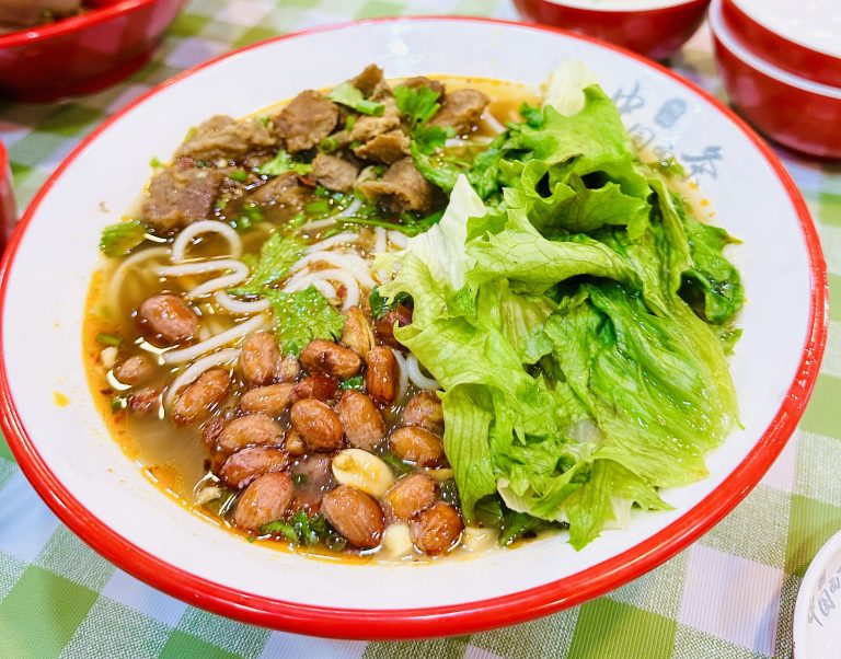 Chinese Keema Noodle
A bowl of Chinese Keema noodles, tender slices of beef, roasted peanuts, and fresh lettuce, garnished with cilantro and served in a red-rimmed bowl on a checkered tablecloth.