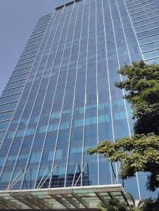 A tall, modern glass skyscraper rises against a clear blue sky. 