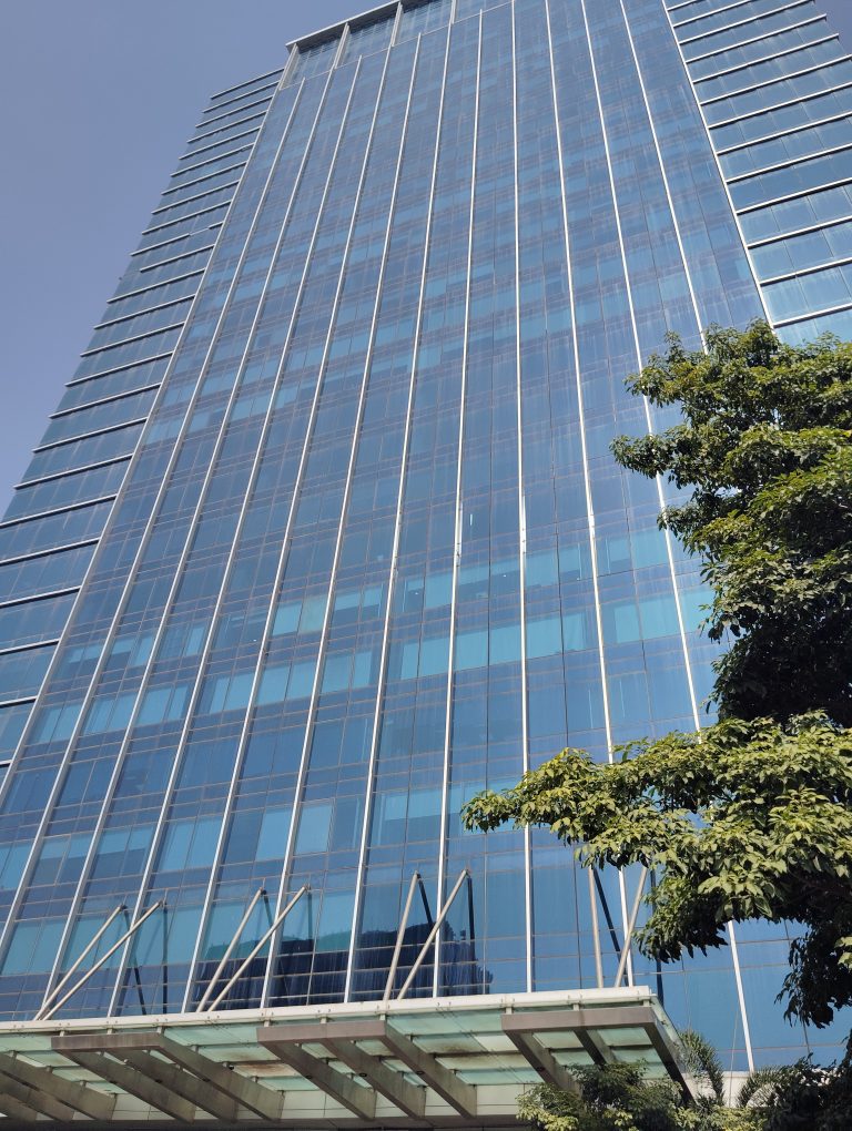 A tall, modern glass skyscraper rises against a clear blue sky.