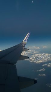 View from an airplane window showing a wing against a backdrop of a clear sky and scattered clouds below.