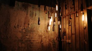 A wall adorned with an assortment of bottles hanging in various arrangements, creating a unique decorative display.
