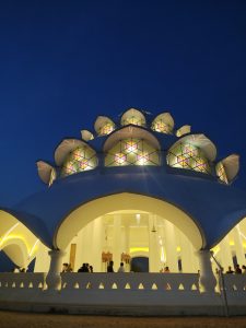 A serene, illuminated dome structure, showcasing intricate stained-glass patterns against a deep blue twilight sky.