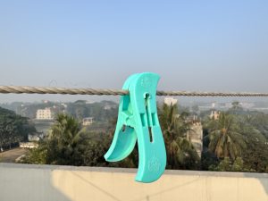 A turquoise plastic clothespin clipped onto a rope clothesline, with palm trees and city buildings visible in the misty morning background.
