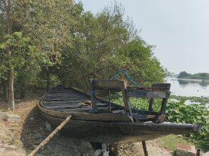 A wooden boat resting on the shore beside a lush green riverbank.