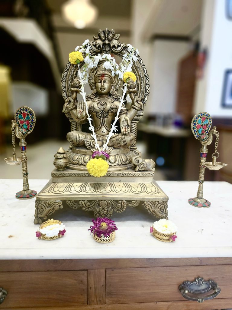 Brass statue of goddess Lakshmi with flowers, garland and two traditional lamps.