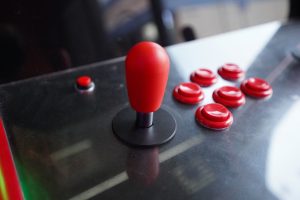 Close-up of an arcade console featuring a red joystick and several red buttons on a reflective surface.