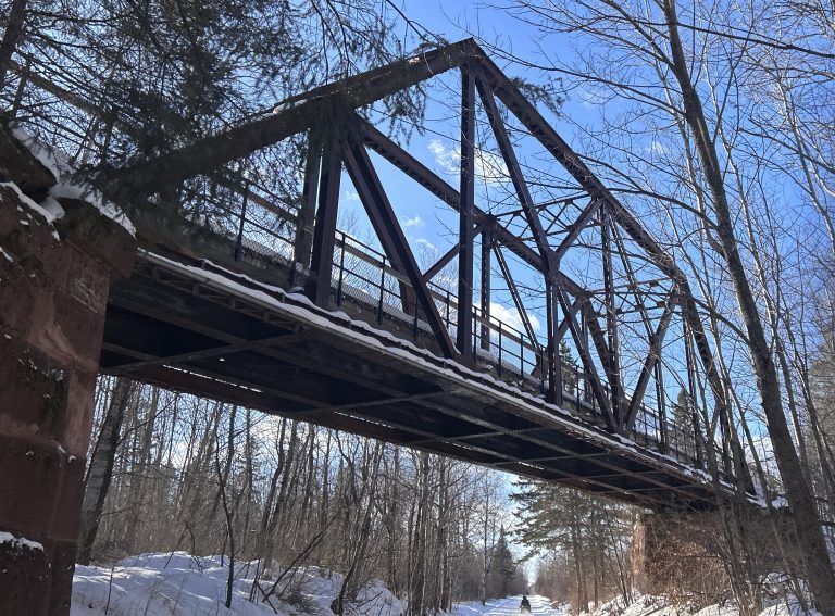 Railroad bridge in woods that are covered in snow. Snowmobile trail going under bridge.