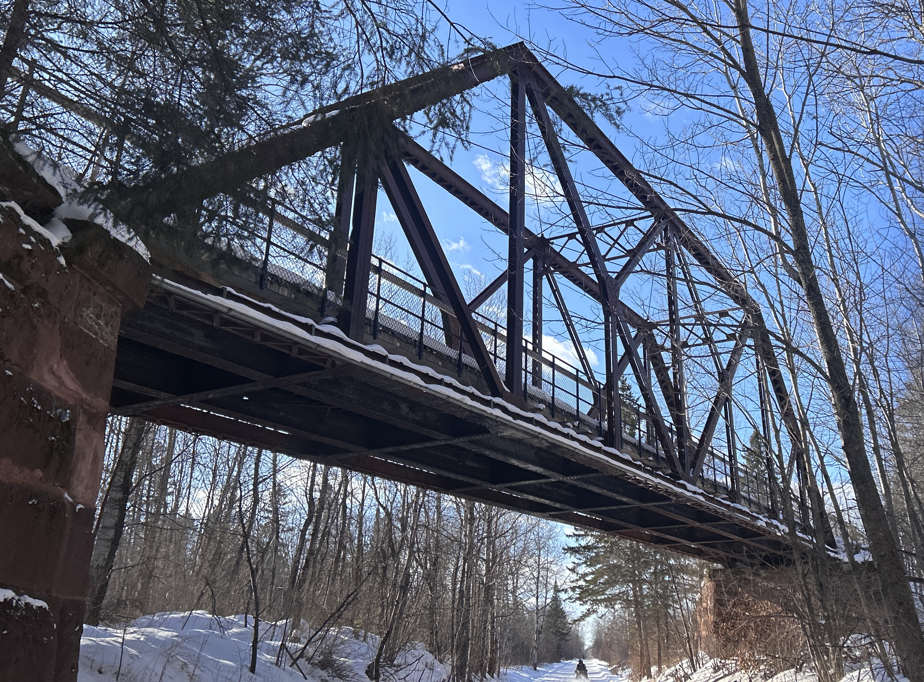 Railroad bridge in woods that are covered in snow. Snowmobile trail going under bridge. 