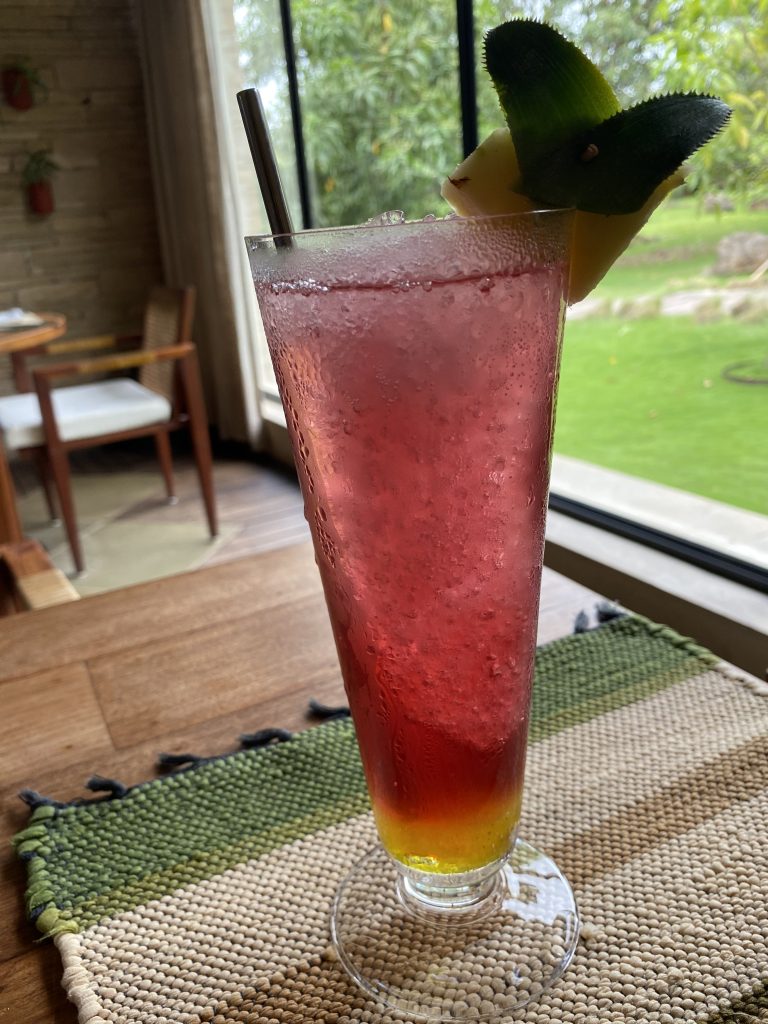 A tall glass filled with a red and yellow gradient beverage, topped with ice cubes.