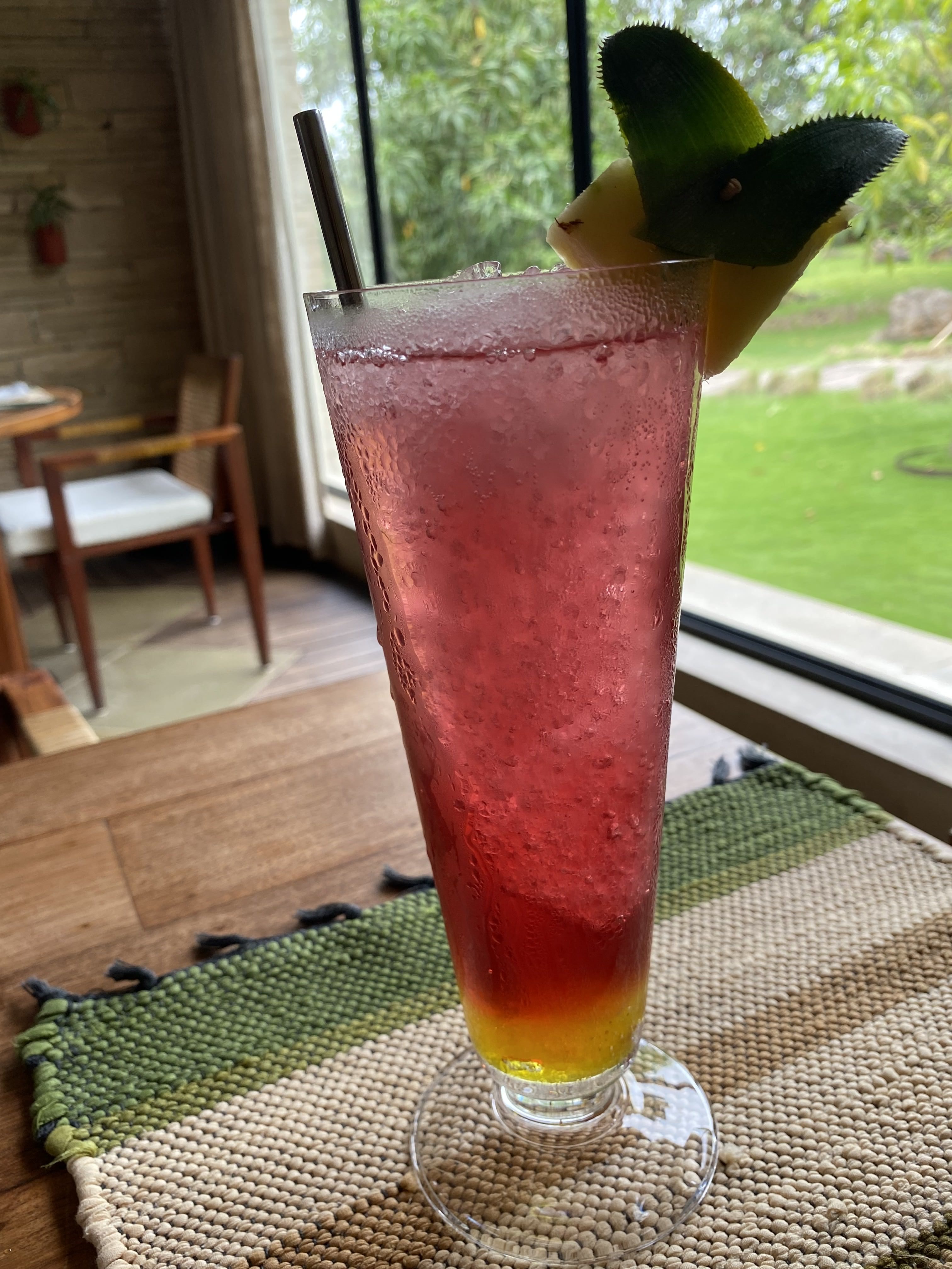 A tall glass filled with a red and yellow gradient beverage, topped with ice cubes. 