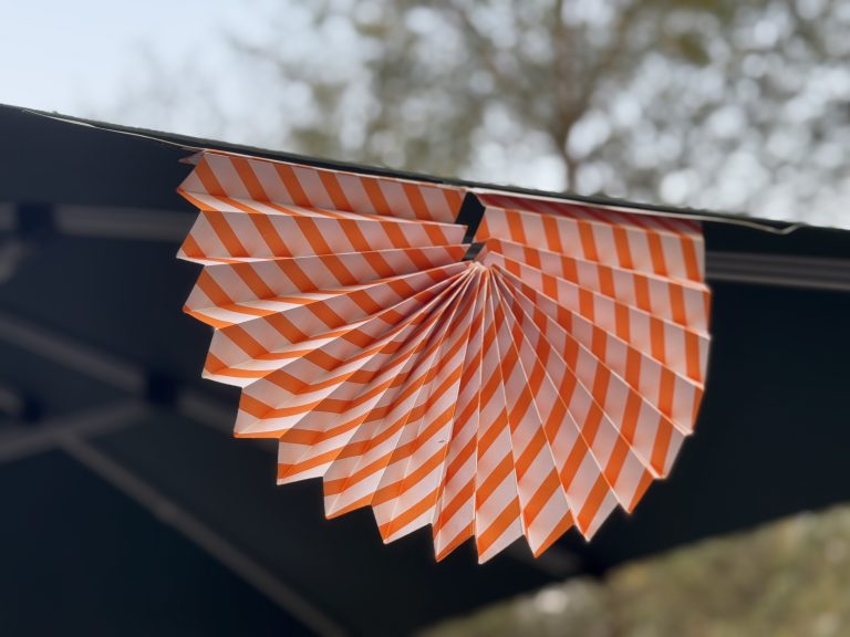 An orange and white striped paper fan elegantly hangs from the ceiling of a tent, adding a vibrant touch to the decor.