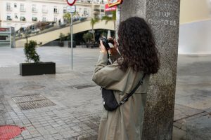 Woman in a trench coat taking photos with a DSLR camera on a city street.