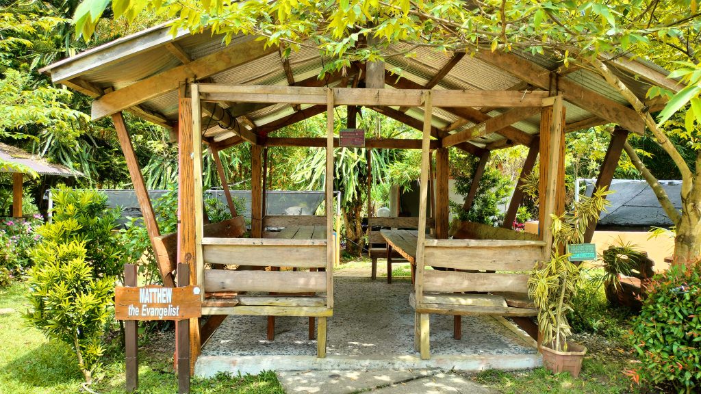 A charming wooden hut named “Matthew the Evangelist” offers a peaceful resting spot surrounded by greenery.