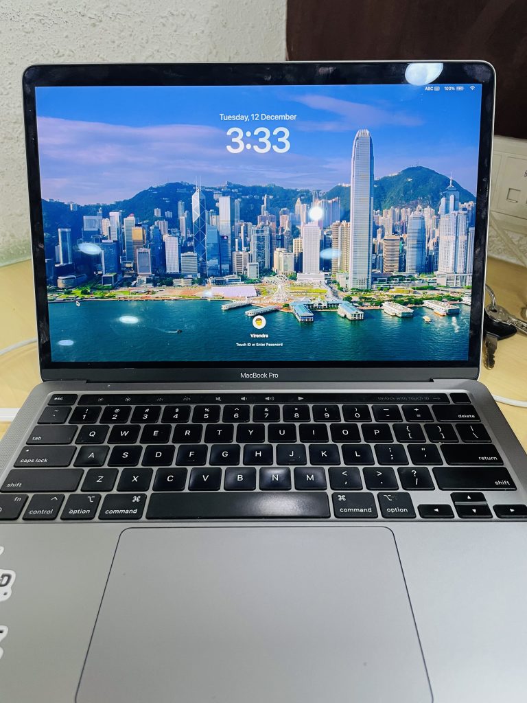 MacBook Pro laptop displaying a cityscape wallpaper with the time 3:33 on the lock screen