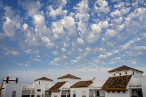 White houses with brown-tiled roofs under a blue sky filled with scattered, fluffy clouds.