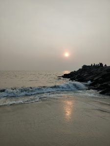 A serene beach scene at sunset, with gentle waves lapping against the shore. The sun is low on the horizon, casting a warm glow on the water.