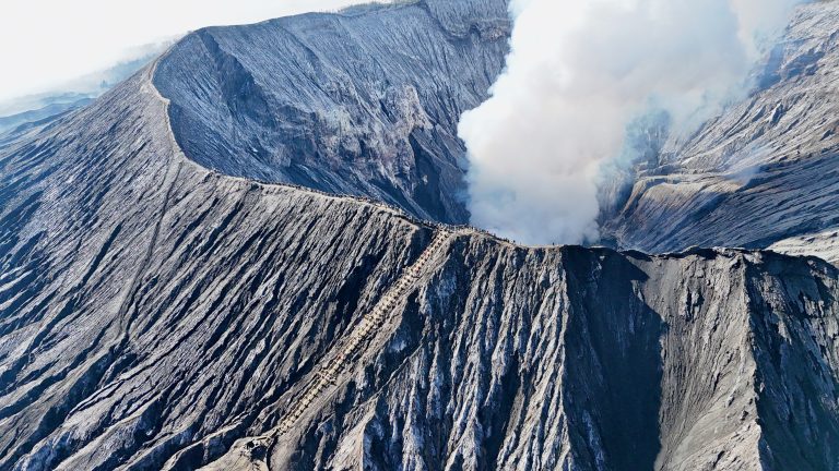 Aerial view of Mount Bromo’s crater with smoke rising from within, capturing the staircase leading up to the volcano