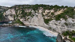 Diamond Beach, Nusa Penida, showcasing towering limestone cliffs covered in green vegetation.