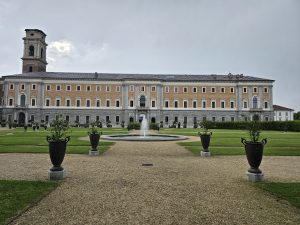 The Royal Palace of Turin (Palazzo Reale) with its gardens (Giardini Reali) and the Galleria Sabauda. The palace is a large, symmetrical building with a tower on the left side. It has a pale yellow facade with rows of windows and a dark roof.