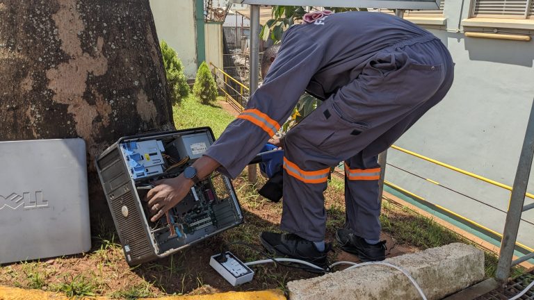 A technician cleaning an old computer by dusting with a blower