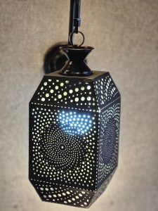 A hexagonal metal downlight with intricate patterns and tiny holes casts a soft glow through the wall in Kozhikode, Kerala.