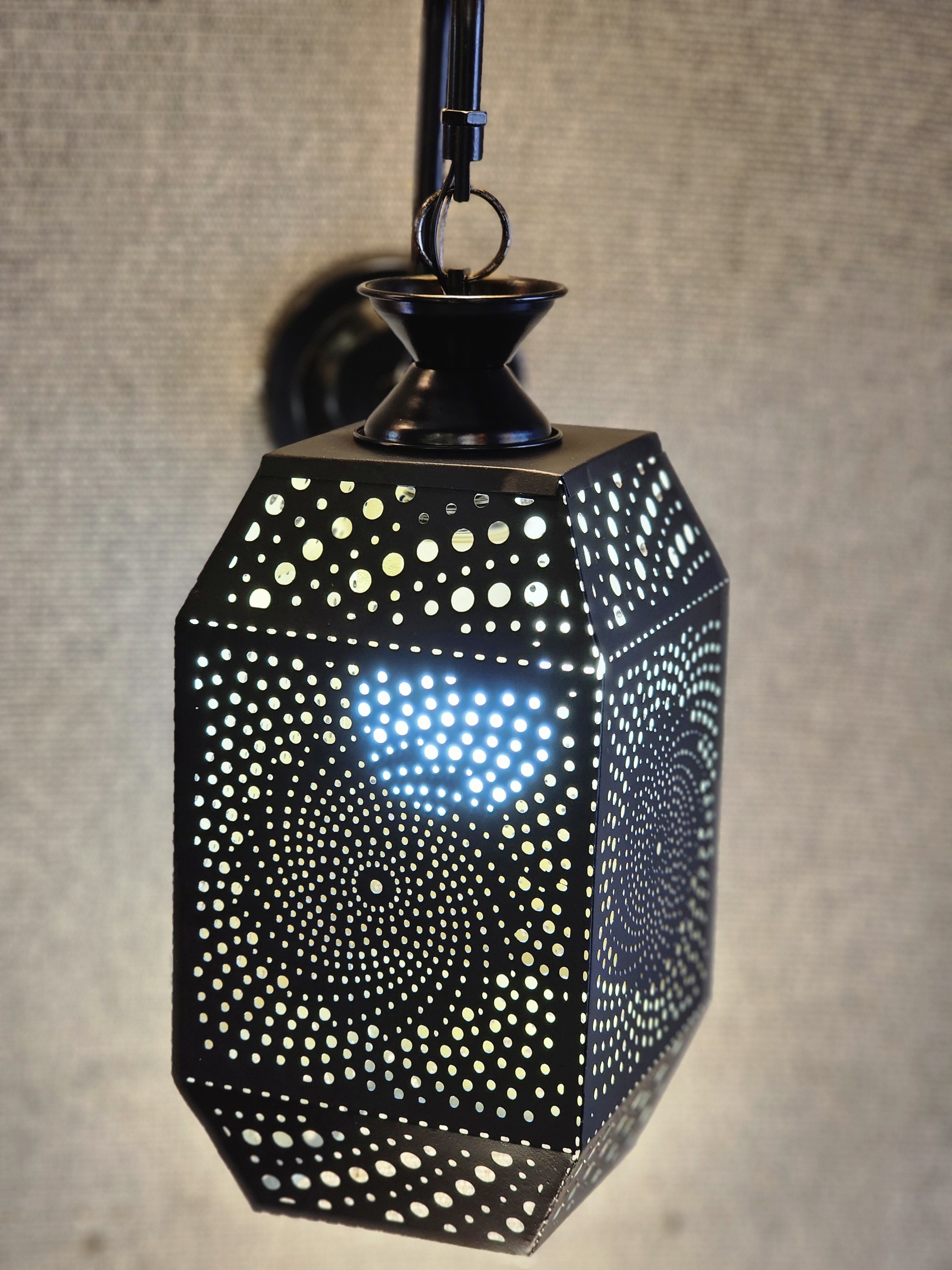 A hexagonal metal downlight with intricate patterns and tiny holes casts a soft glow through the wall in Kozhikode, Kerala.