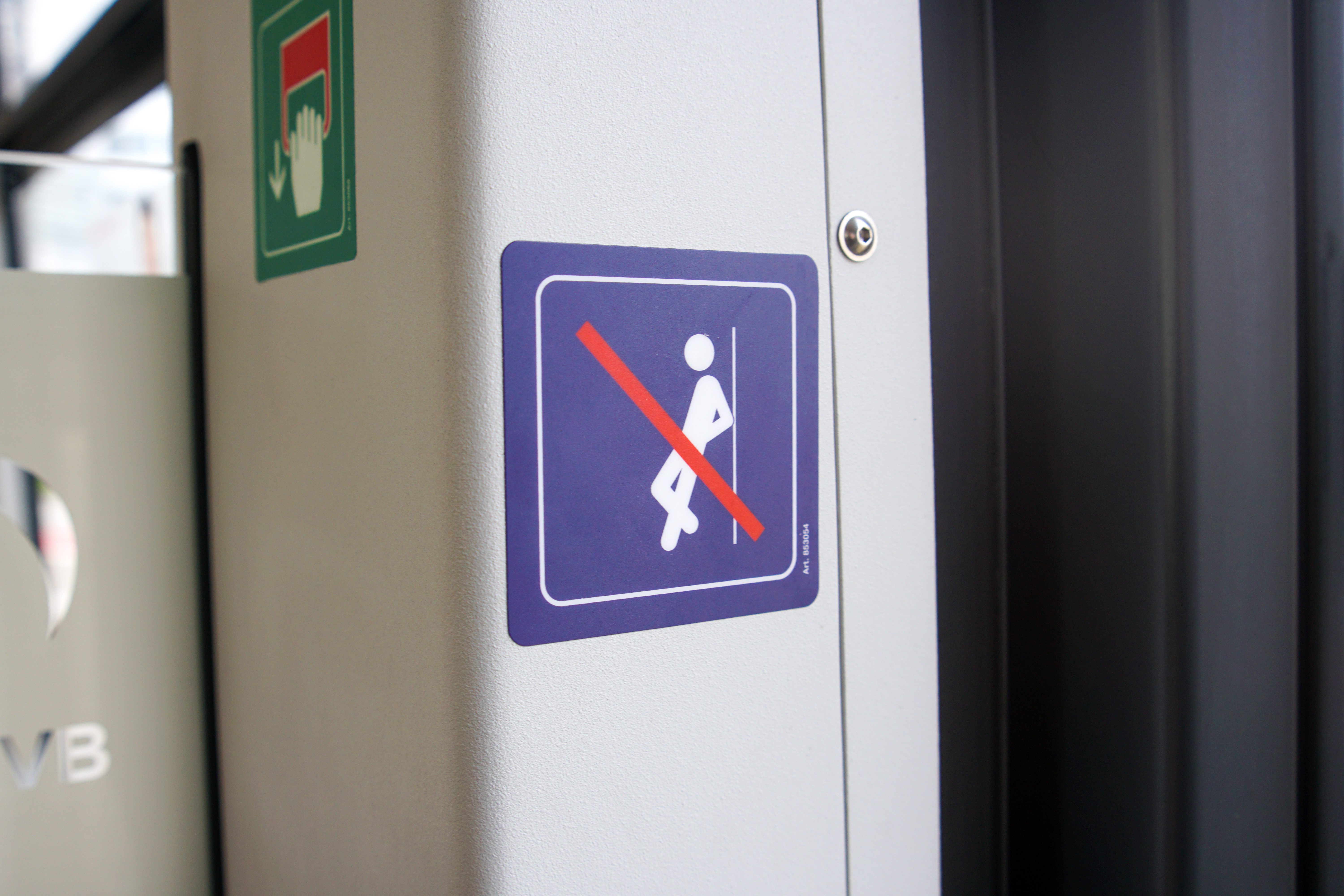 A sign on a train indicating "no leaning" with a figure leaning against a rail, crossed out with a red line.