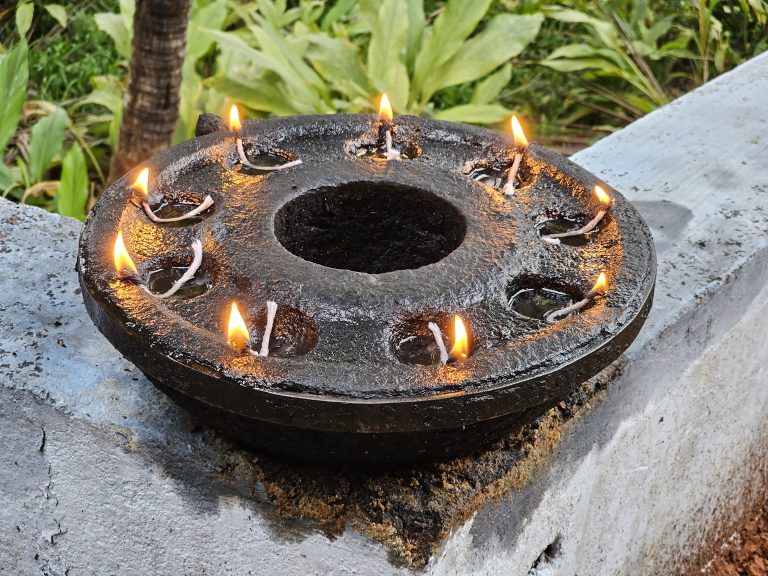 A traditional circular black colour stone oil lamp  with several small reservoirs around its circumference. Each reservoir holds a small amount of oil and a cotton wick, which is lit, creating individual flames.