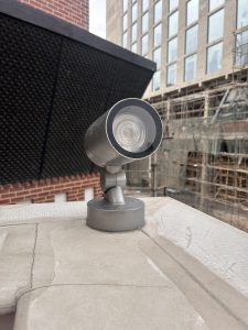 A close-up view of an outdoor security camera mounted on a ledge with an urban building under construction in the background.