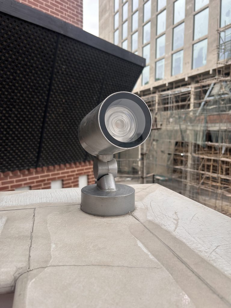 A close-up view of an outdoor security camera mounted on a ledge with an urban building under construction in the background.