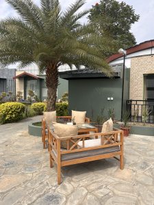An outdoor seating area with wooden furniture and beige cushions arranged around a glass table