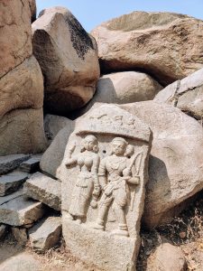 Ancient stone carving depicting two figures standing side by side, one holding a weapon and the other raising a hand, set against a backdrop of large rocks (Lord Ram, Seetha).
