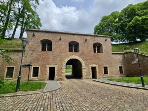 The Cihelná brána, also known as the Brick Gate, at Vyšehrad Castle in Prague, a historical landmark. The gate is constructed of red brick and features an arched passageway in the center, flanked by smaller doorways and windows.