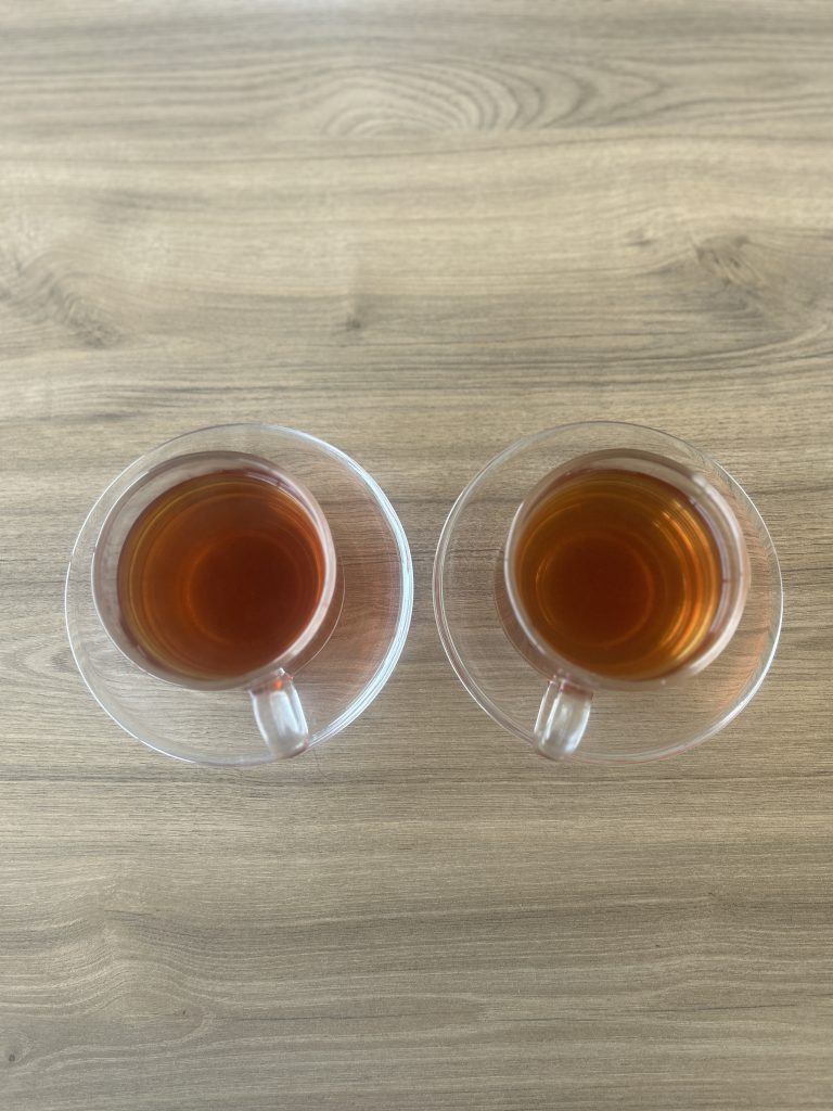 Two cups of tea on saucers placed side by side on a wooden surface.