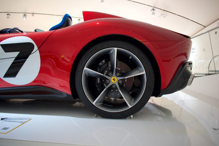 Close-up side view of a red sports car showcasing its rear wheel, sleek bodywork with a racing number 7, and aerodynamic detailing around the exhaust.