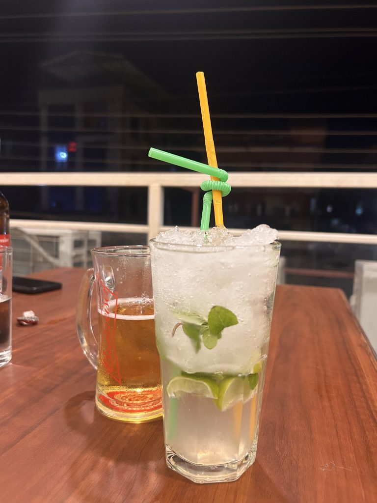 A refreshing drink with lime slices and mint leaves in a glass filled with ice, accompanied by two colorful straws twisted together