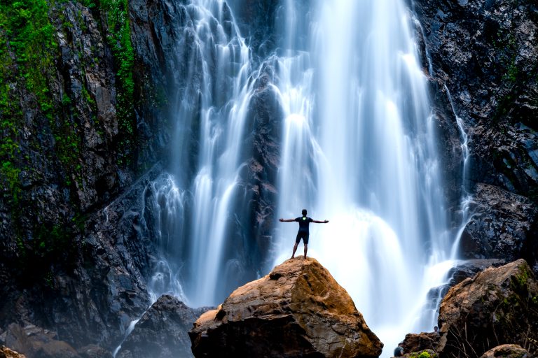 A man standing on a big rock. Waterfall in background. Photo taken at Karnataka, India.