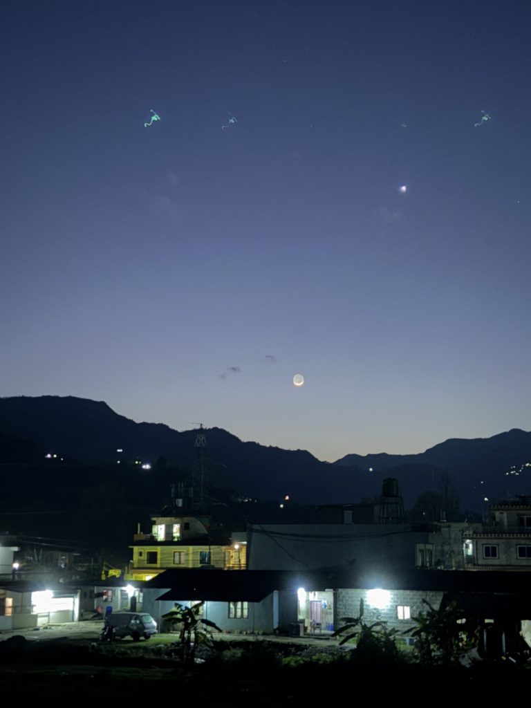 A twilight scene with a crescent moon and a bright star visible in the sky