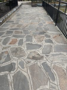 Stone pathway with irregular-shaped stones, flanked by black metal railings on either side.