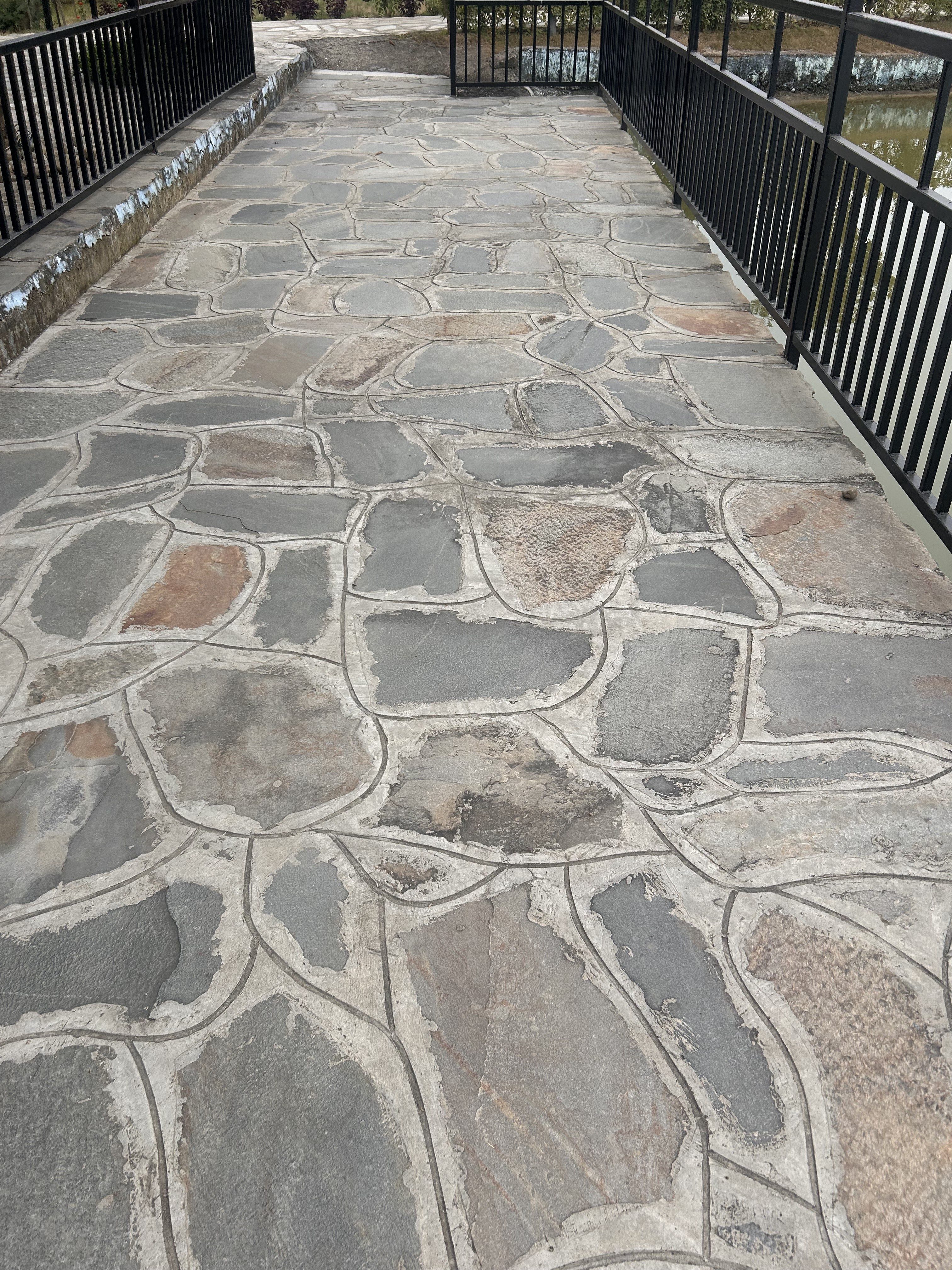 Stone pathway with irregular-shaped stones, flanked by black metal railings on either side.