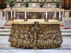 The Altar of Santa Maria ad Martyres, located in the Pantheon in Rome. The altar is adorned with a bronze relief sculpture depicting religious figures. Above the altar, there is a draped cloth and several candles.