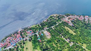 Aerial view of Taal Lake in Tagaytay, Philippines, showing lakeside houses with colorful rooftops nestled among lush greenery. The lake surrounds Taal Volcano, an active volcano situated on an island within the lake.
