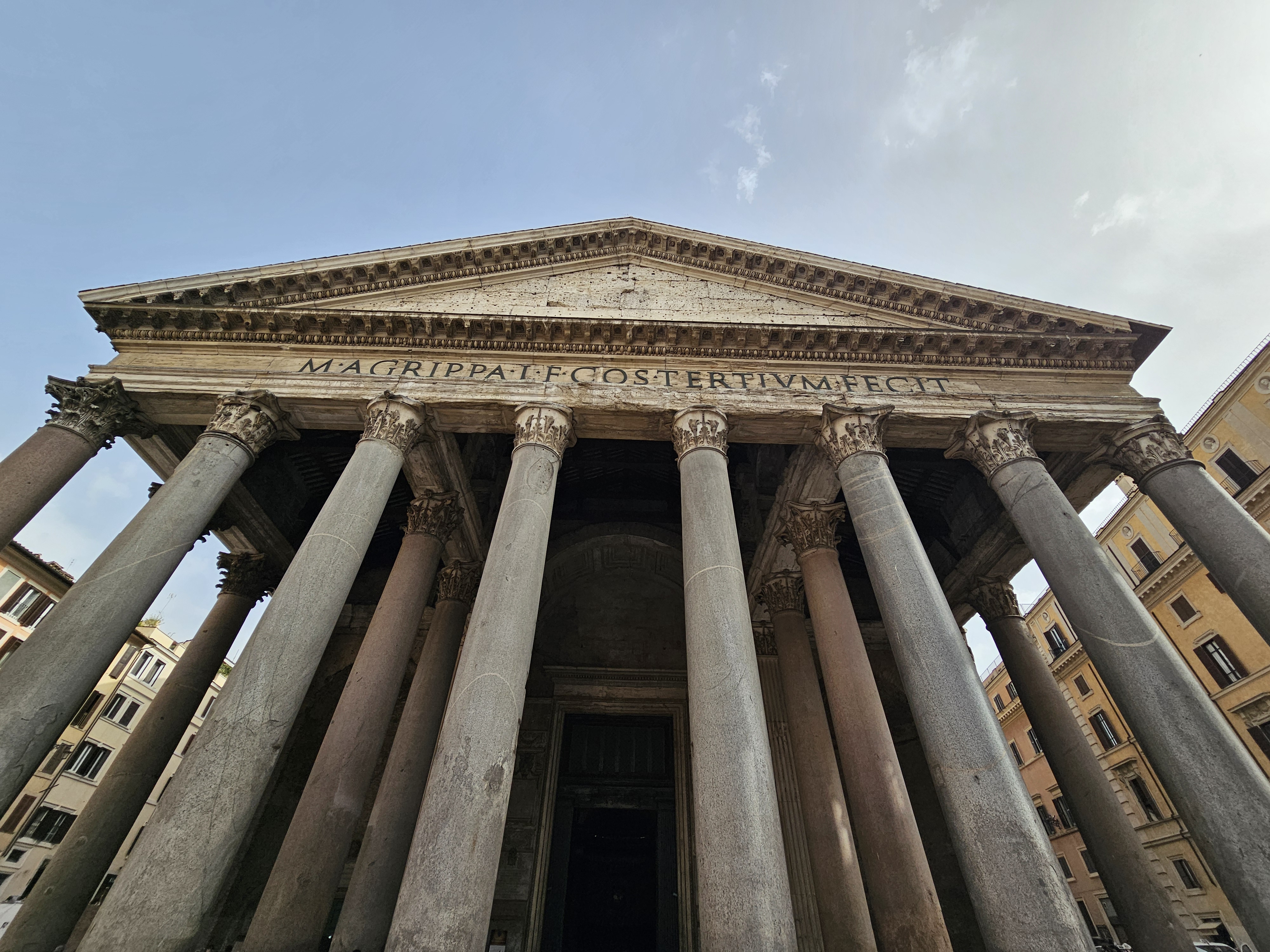 A front view of the Pantheon in Rome, Italy. The structure is an example of ancient Roman architecture, featuring a portico with large granite columns and a triangular pediment. The inscription "M AGRIPPA L F COS TERTIVM FECIT" is visible on the frieze, indicating its construction by Marcus Agrippa.