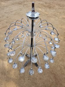 A traditional metal lamp used in a temple in Kozhikode, Kerala. It has curved metal rods extending from a central pole, each holding small cups for oil lamps.