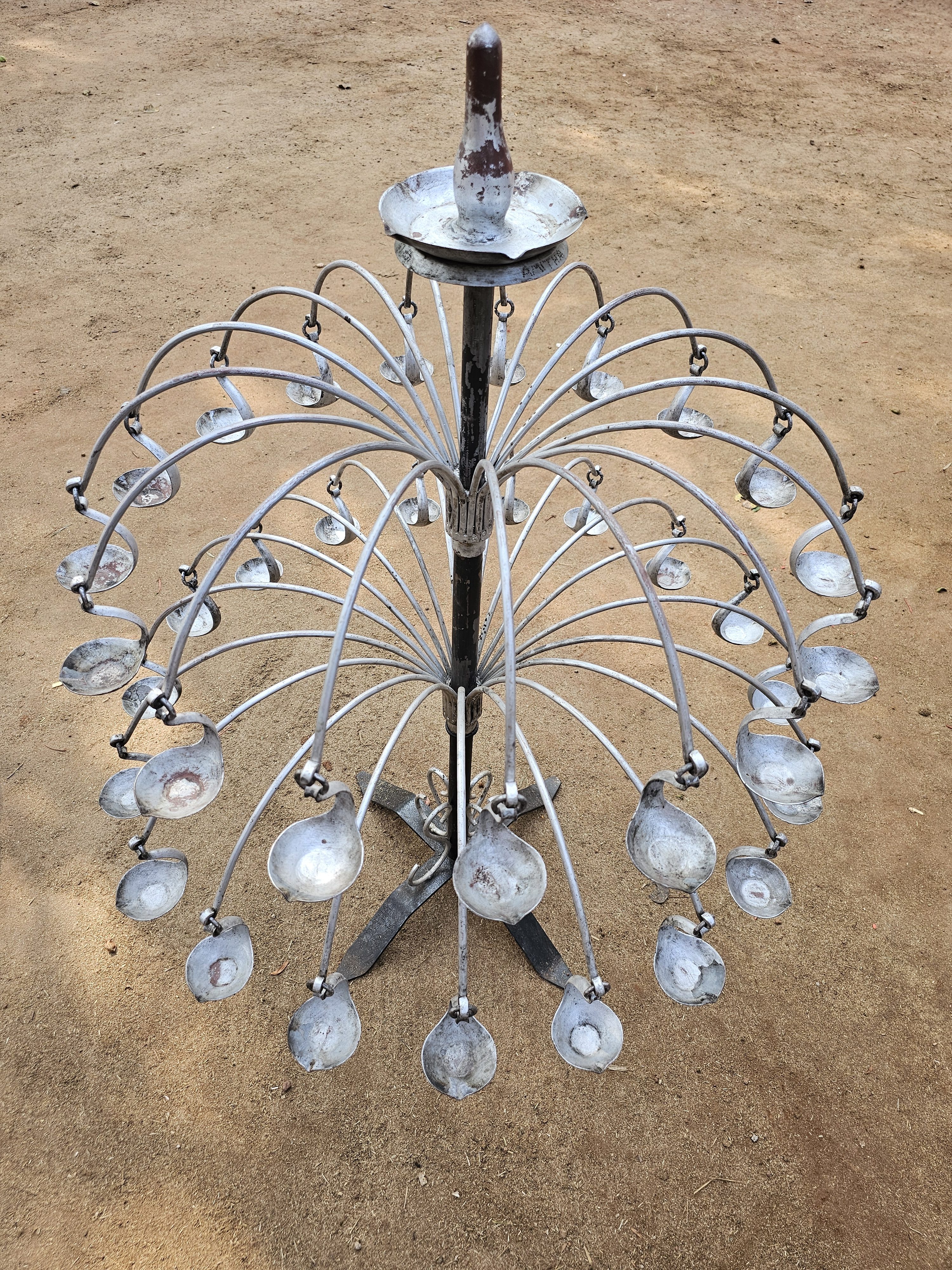 A traditional metal lamp used in a temple in Kozhikode, Kerala. It has curved metal rods extending from a central pole, each holding small cups for oil lamps.
