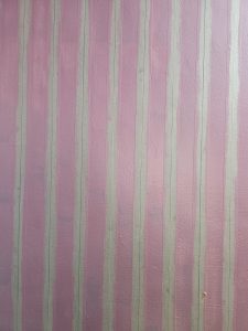 A textured wall, painted pink and marked with white masking tape stripes, is undergoing preparation for a striped paint finish. Captured from Perumanna, Kozhikode, Kerala. 