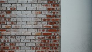  A textured brick wall featuring a section of white wall and a prominent red brick among the bricks.