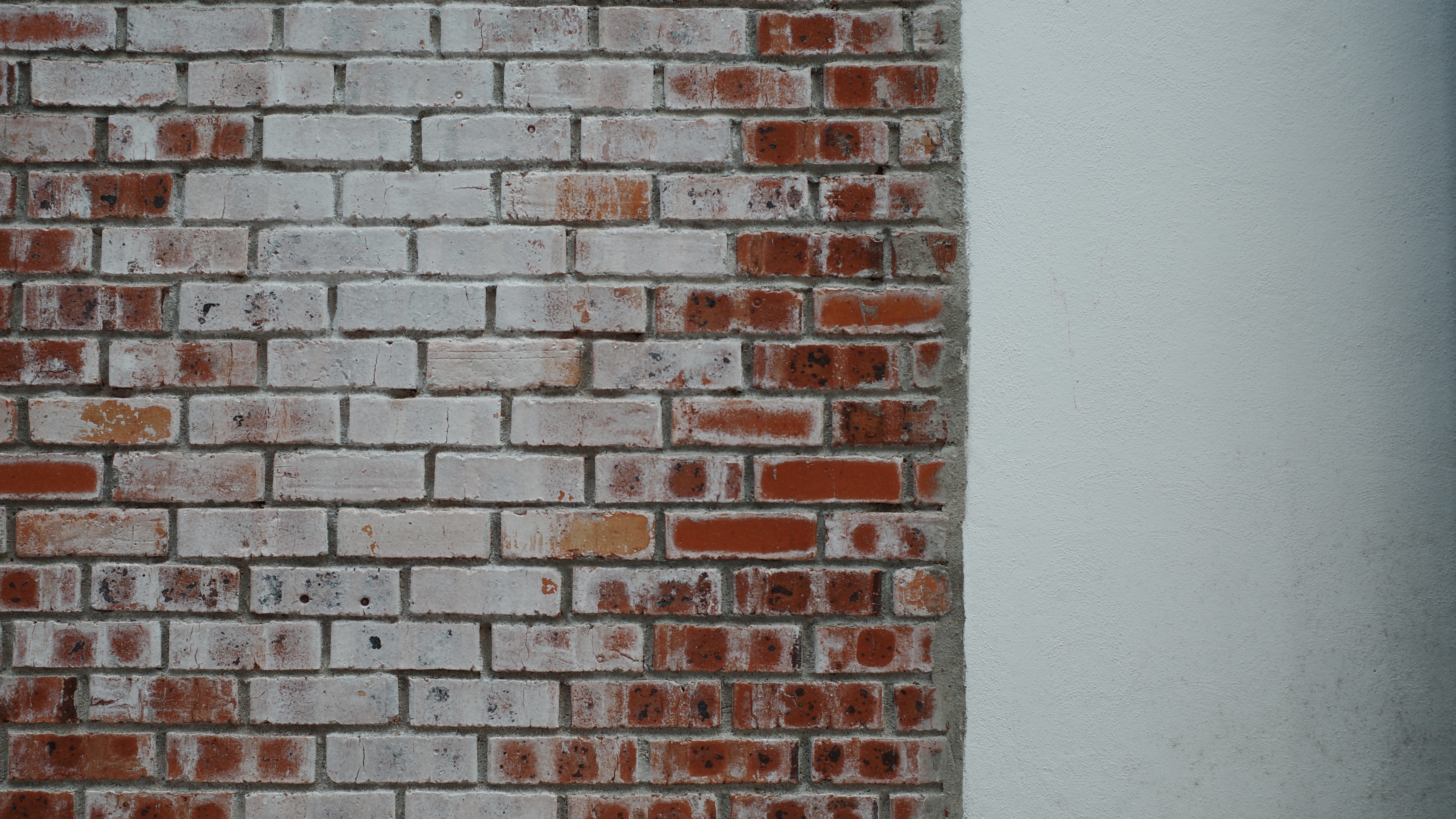 A textured brick wall featuring a section of white wall and a prominent red brick among the bricks.