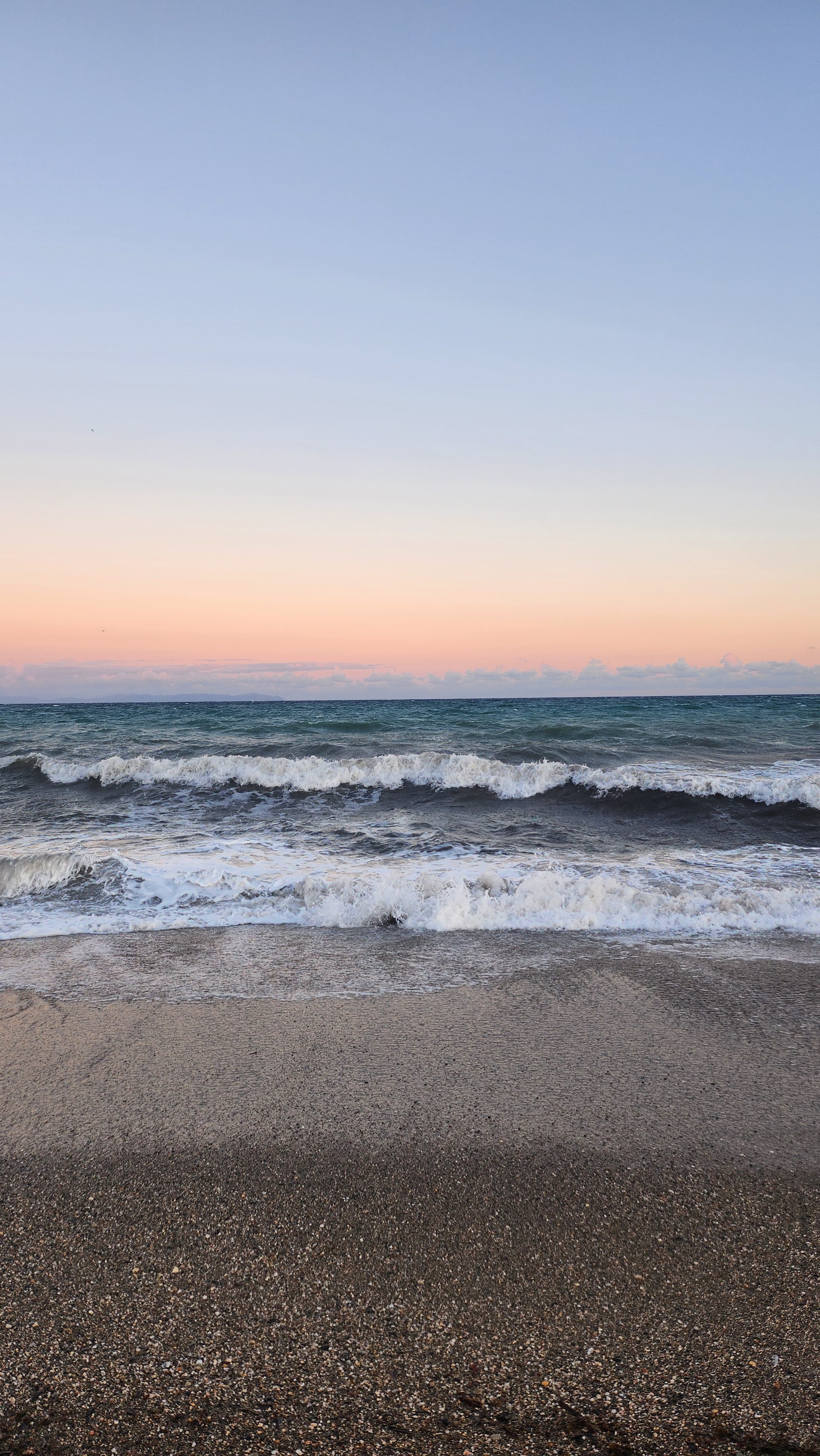 A tranquil seascape featuring waves crashing onto a sandy beach, with a soft pastel sky transitioning from pink to blue at sunset.